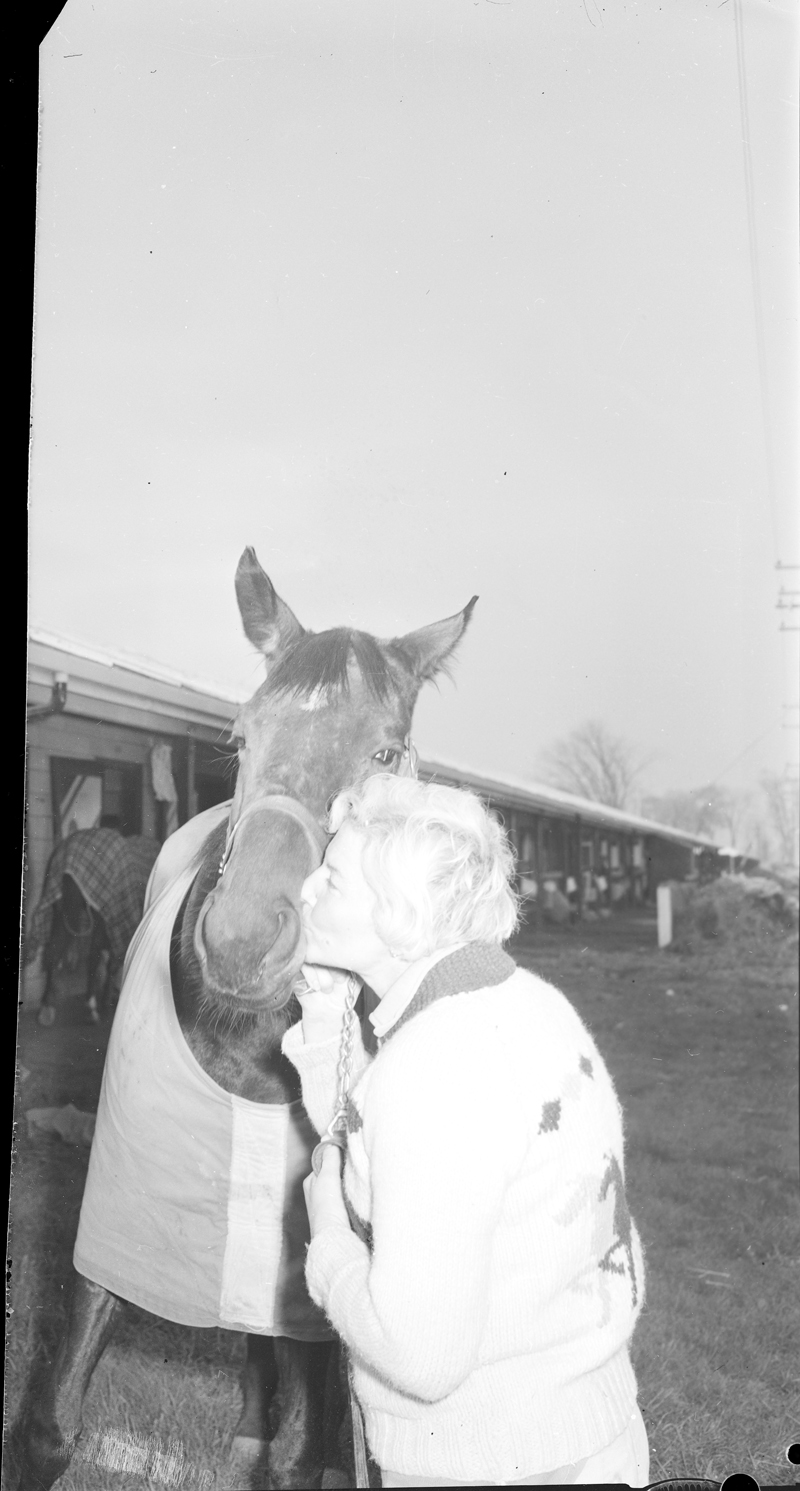 Image of woman kissing horse's nose by stables at New Woodbine Racetrack, 1959. Image no. ASC03645.